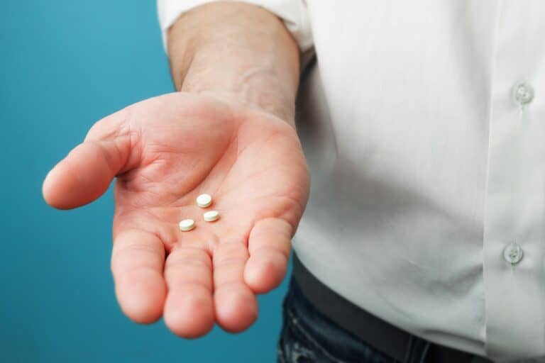 man holding three small white pills