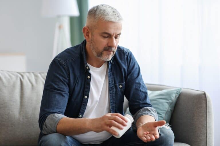 old man holding pills sitting on sofa